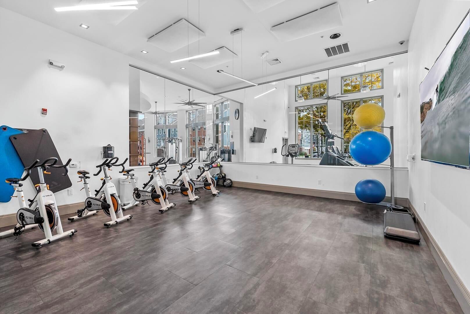 Een fitnessruimte met hometrainers, een spiegel en fitnessballen.
