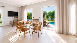 Un'ampia stanza con zona pranzo, TV a schermo piatto e vista su una piscina.