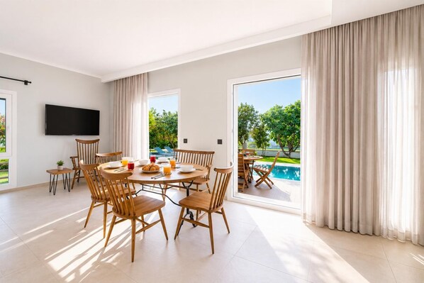 Ein geräumiges Zimmer mit Essbereich, einem Flachbildfernseher und Blick auf einen Swimmingpool.