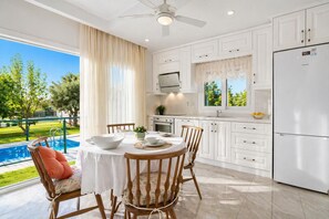A modern kitchen with white cabinets, a dining table with chairs, a refrigerator, and a view of a swimming pool.