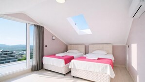 A bedroom with two beds, a skylight, a large window, and a view of buildings. - Villa Riva - Three Bedroom Villa, Sleeps 6 (Oludeniz)