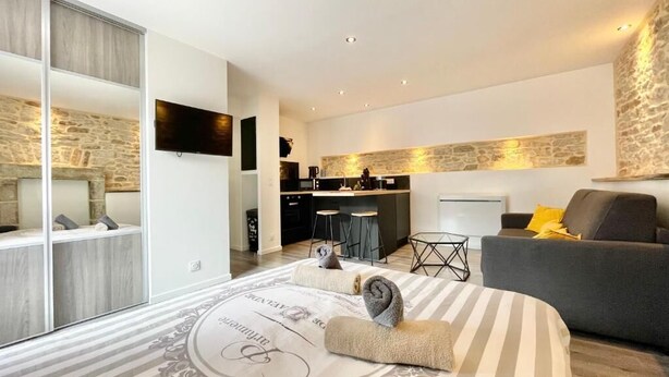 A modern living room with a sofa, a dining area with a kitchen, and a large bed with a decorative headboard. - 4★ Renovated Studio with Wifi, 5 min Walk to Quimper Station (Quimper)