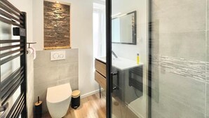 A modern bathroom with a glass shower enclosure, a wooden vanity, and a stone accent wall. - 4★ Renovated Studio with Wifi, 5 min Walk to Quimper Station (Quimper)