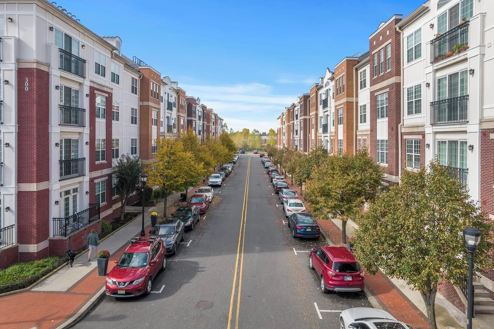 A row of townhouses with a central road, parked cars, and trees lining the street.