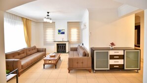Ein modernes Wohnzimmer mit einer Couch, einem Couchtisch und einem Kamin. Ein Fernseher und eine Kommode mit Schubladen sind ebenfalls vorhanden.