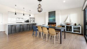 Une cuisine moderne dotée d’un îlot central, de tabourets de bar, d’une table à manger avec des chaises, de luminaires suspendus, d’une cheminée et d’une décoration sur le thème de la voile.