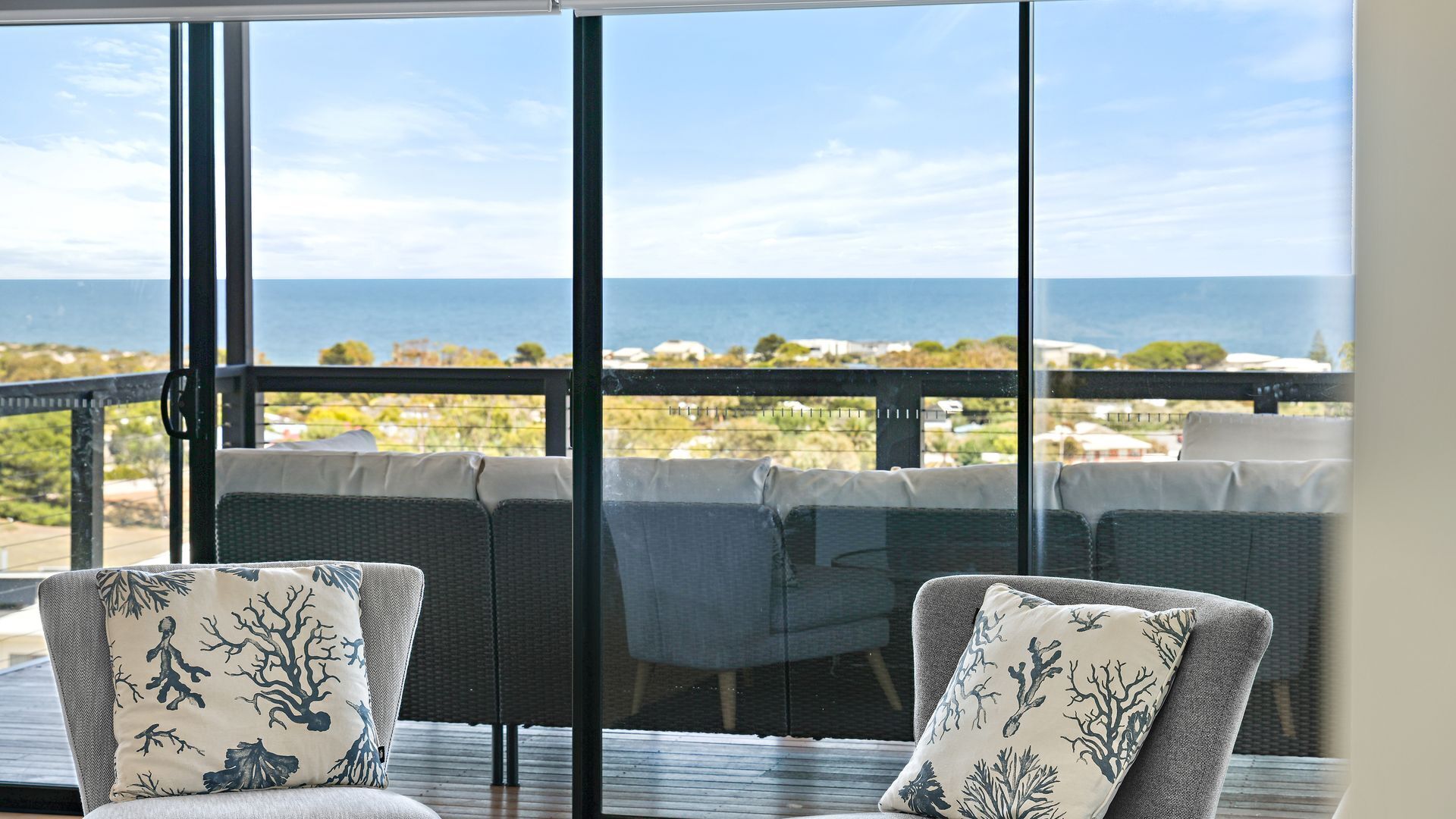 A balcony with a view of the sea, wicker furniture, and a table.