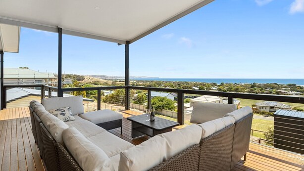 Un espace extérieur aménagé, abrité et doté de mobilier en osier, d’une petite table et offrant une vue sur l’océan et le paysage environnant.