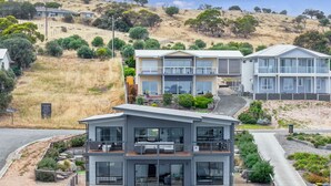 Une maison moderne à deux étages, dotée d’un balcon, entourée d’un jardin aménagé et d’un paysage vallonné.