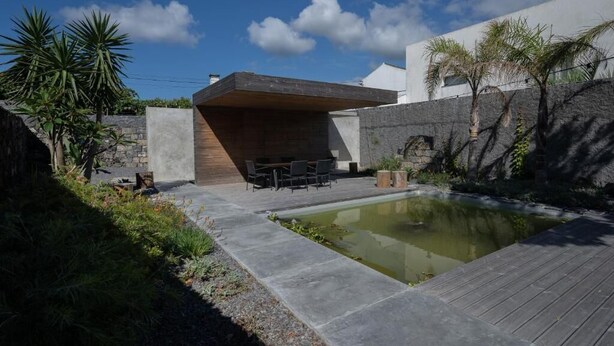 A modern outdoor patio with a pool, stone walls, and a wooden deck. - North Shore Hostel (Ribeira Grande)