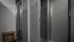 A bathroom with a glass shower enclosure, a wooden stool, and a plain wall. - North Shore Hostel (Ribeira Grande)