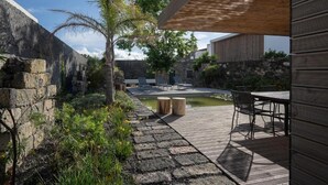 A wooden deck with a stone wall, a small pond, and outdoor seating. - North Shore Hostel (Ribeira Grande)