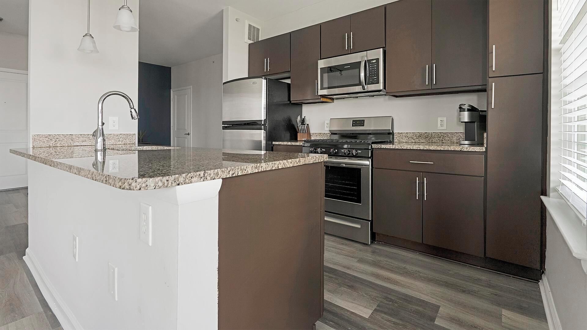 A modern kitchen with dark brown cabinets, stainless steel appliances, and a granite countertop island.