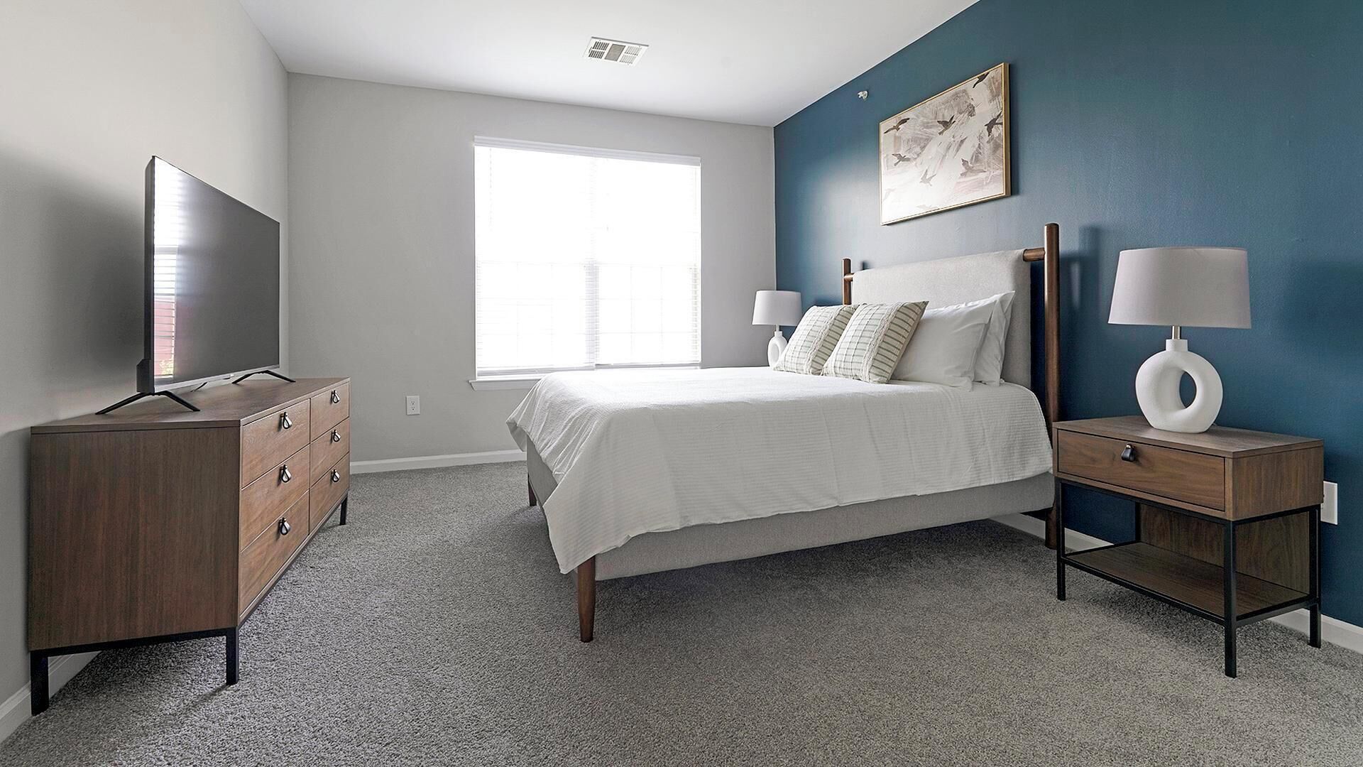 A bedroom with a bed, dresser, nightstands, a TV, and a window.