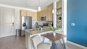 A modern kitchen with stainless steel appliances, a granite countertop, and a dining area with a wooden table and chairs. - Landing | Spectacular 1BD, Yoga Studio, Pool (Anna)