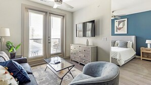 A modern bedroom with a bed, a TV, a dresser, and a chair. - Landing | Spectacular 1BD, Yoga Studio, Pool (Anna)