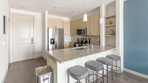 Una cocina moderna con una isla central, electrodomésticos de acero inoxidable y taburetes de bar.