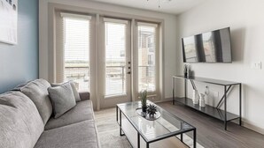 Una sala de estar moderna con un sofá, una mesa de centro de vidrio y un televisor montado en la pared.