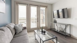 Ein modernes Wohnzimmer mit einer Couch, einem Glastisch und einem an der Wand befestigten Fernseher.