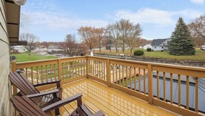Eine Holzterrasse mit Geländer, mit Blick auf ein Gewässer und eine Wohngegend mit Häusern und Bäumen.