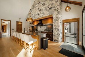 A modern kitchen with a stone wall, wooden bar, and stainless steel appliances. - New! Modern Lake Area Home w/ Hot Tub! (Oakland)