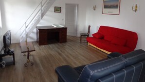 Een woonkamer met een trap, een rode bank, een houten bureau en een televisie.
