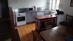 Een compacte keuken met witte apparaten, een houten eettafel en een raam dat voor daglicht zorgt.