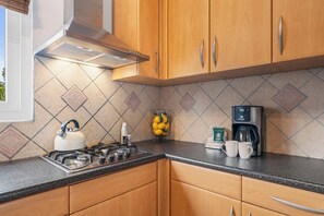 A kitchen with wooden cabinets, a gas stove, a kettle, a coffee maker, and a fruit bowl. - 3BR Pool Villa w/ Golf Views, Tierra del Sol (Noord)
