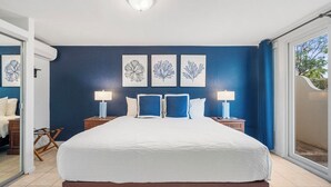 Une chambre d’hôtel avec un grand lit, deux tables de chevet avec des lampes et une vue sur l’extérieur, accessible par une porte-fenêtre coulissante.