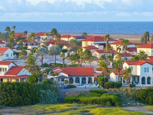 Ein Küstenwohngebiet mit Häusern mit roten Dächern, umgeben von Palmen und Blick auf das Meer.