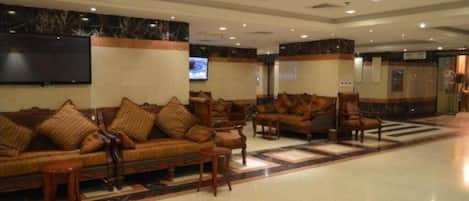 A lobby with sofas and armchairs, a flat-screen TV, and a tiled floor.