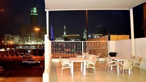 Een balkon met een tafel en stoelen, met uitzicht op een verlicht stadsbeeld 's nachts.