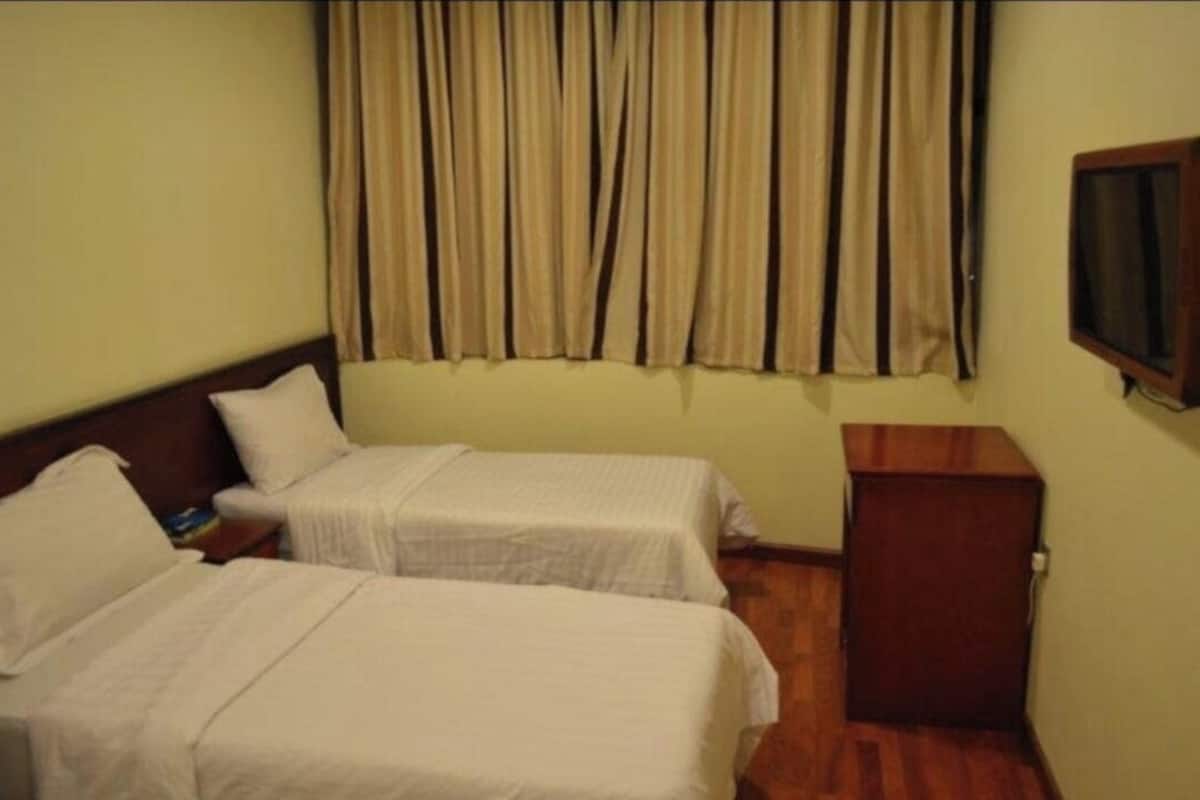 Ein Hotelzimmer mit zwei Einzelbetten, einem Holfnachtkästchen, einem Fernseher und einem Vorhang.
