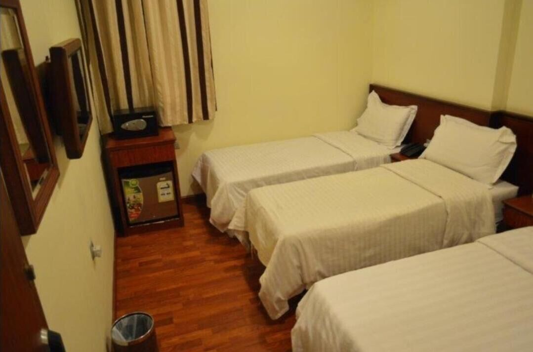 A small hotel room with two single beds, a wooden floor, a small table with a radio, and a trash bin.