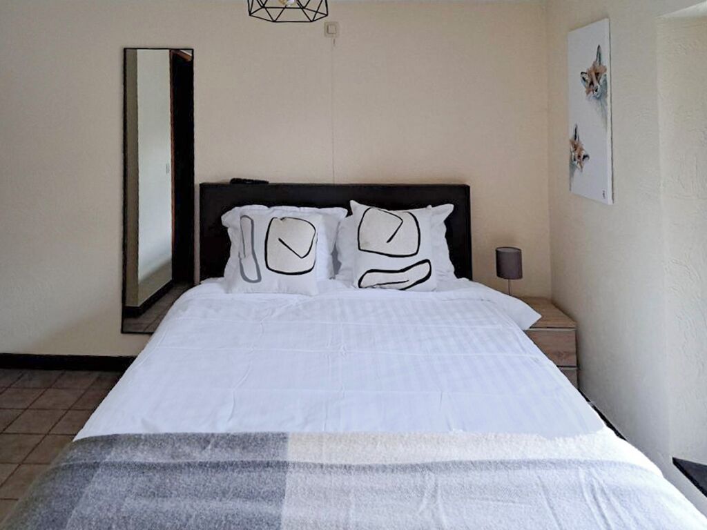 Habitación de hotel con cama, mesita de noche, espejo adosado a la pared y un cuadro enmarco.