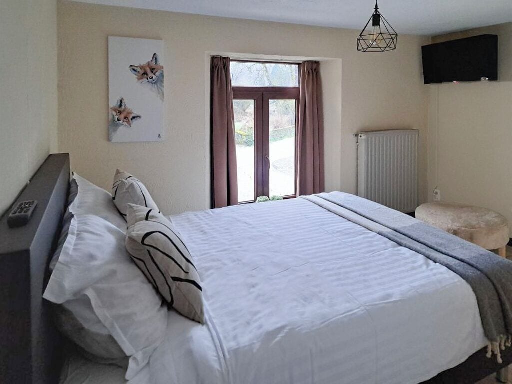 Een slaapkamer met een groot bed, een nachtkastje, een stoel, een radiator en een raam met gordijnen.