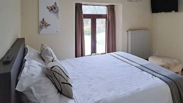 Een slaapkamer met een groot bed, een nachtkastje, een stoel, een radiator en een raam met gordijnen.