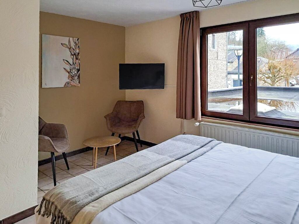 Une chambre d’h ôtel avec un lit, une chaise, une petite table, un tableau au mur et une fenêtre avec des rideaux.