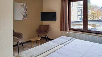 A hotel room with a bed, a chair, a small table, a painting on the wall, and a window with curtains.