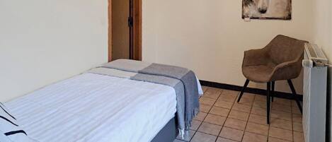 A bedroom with a bed, a chair, a radiator, and a wall painting.