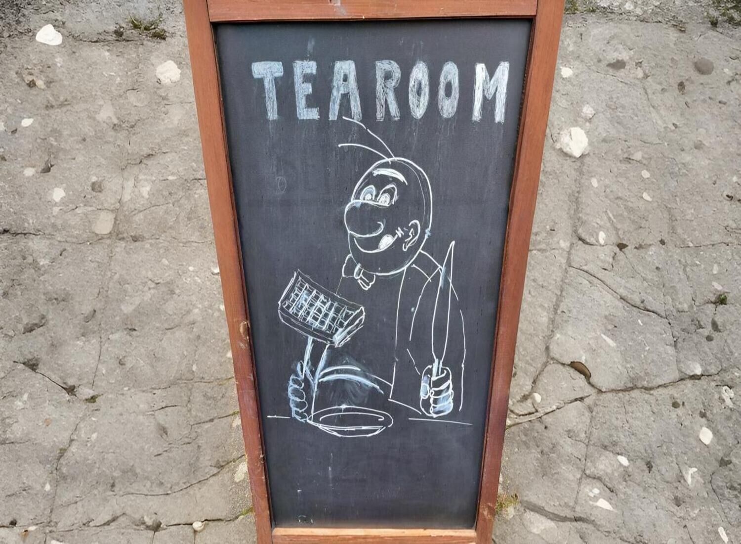 A chalkboard sign with the word "TEAROOM" and a drawing of a person with a telescope and a plant.