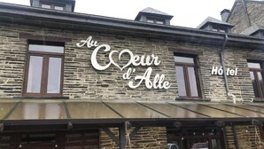 En hotellfasad med en stenfasad och en skylt med texten ”Au Coeur d’Alle”.