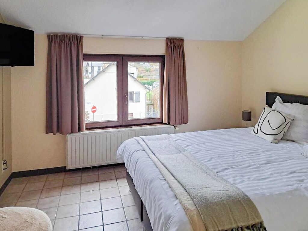 Un dormitorio con cama, ventana con cortinas, radiador y televisor en la pared.