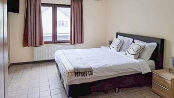 A bedroom with a bed, curtains, a radiator, a window, and a bedside table.