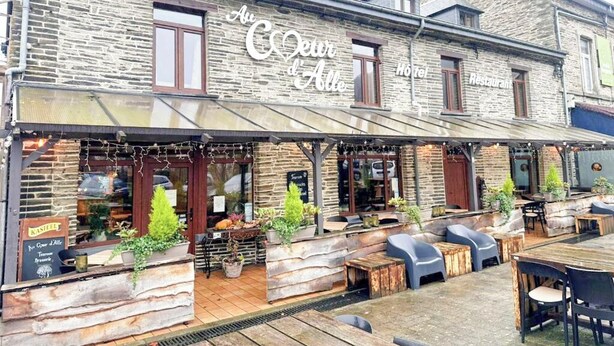 En byggnad i sten med en skylt som lyder: ”Au Coeur d’Alle – hotell och restaurang”.