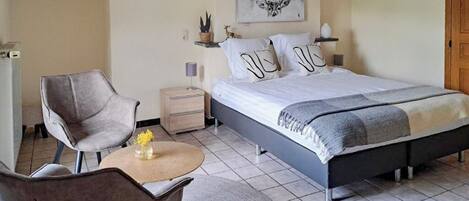 A bedroom with a bed, two bedside tables, a chair, a small table with a vase, and a wall-mounted artwork.