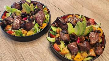 Due ciotole di insalata con carne alla griglia, verdure e avocado.