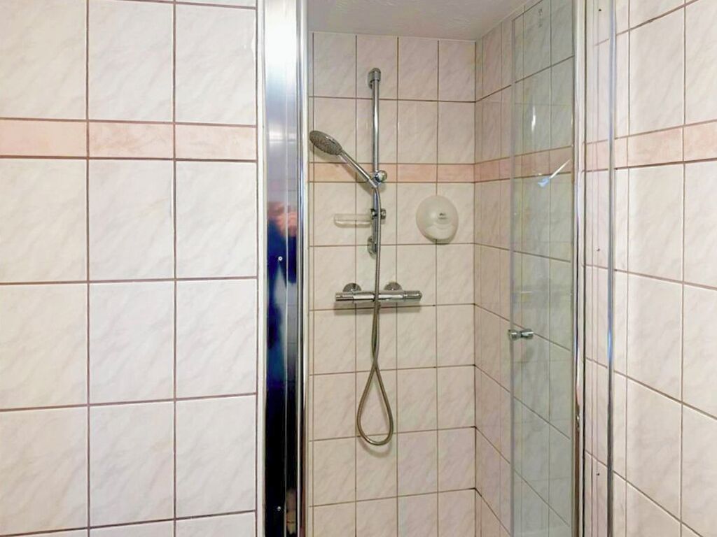 A shower with a handheld showerhead and a wall-mounted control panel.