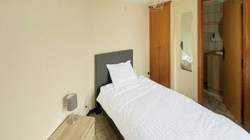 A bedroom with a single bed, a wooden nightstand, a wall-mounted lamp, and a wooden wardrobe.
