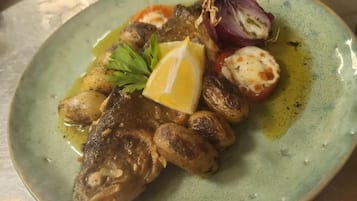 A plate with a fish, potatoes, tomatoes, and a lemon wedge.